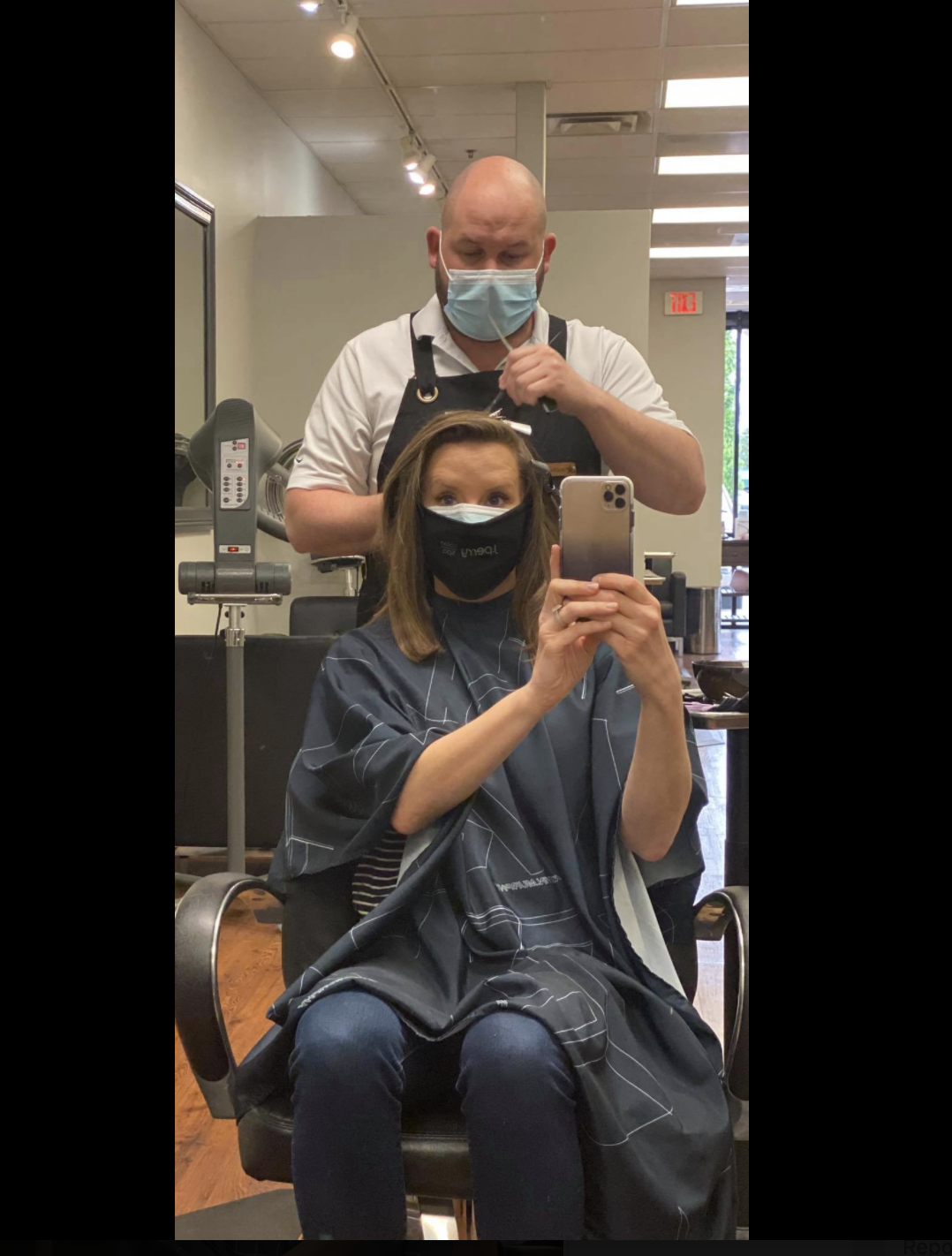 Image of woman getting her hair cut. The woman and man are both wearing small medical facemask.
