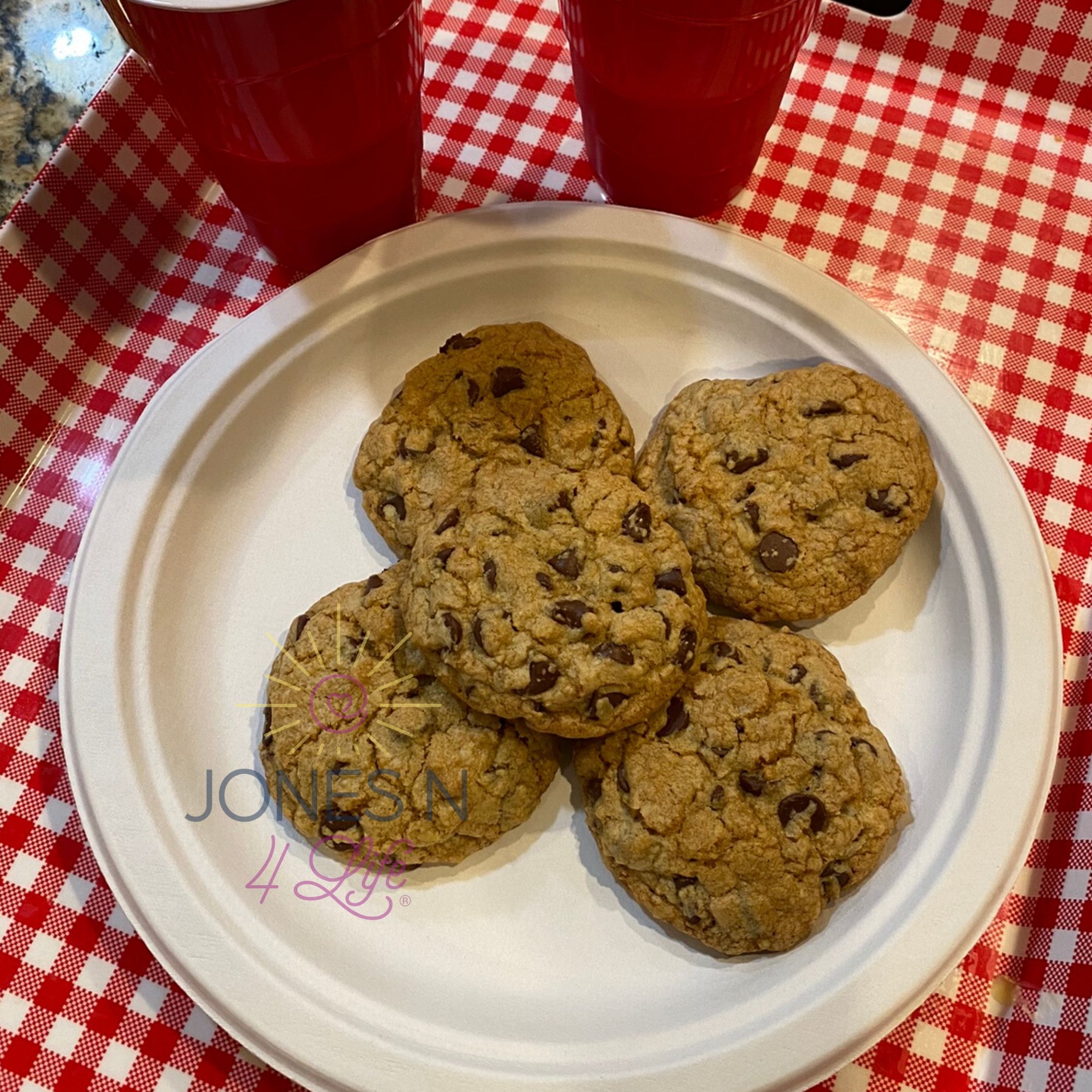 Chocolate chip cookies on a white paper place on top of red an white checkered tray.